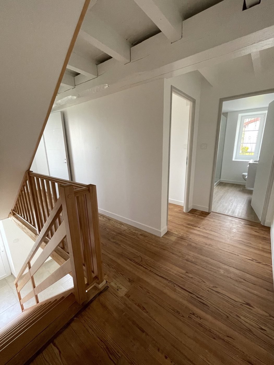 Le cachet de l'ancien préservé : poutres apparentes, parquets d'origine, escalier en bois — chaque rénovation respecte l'âme du bâti.